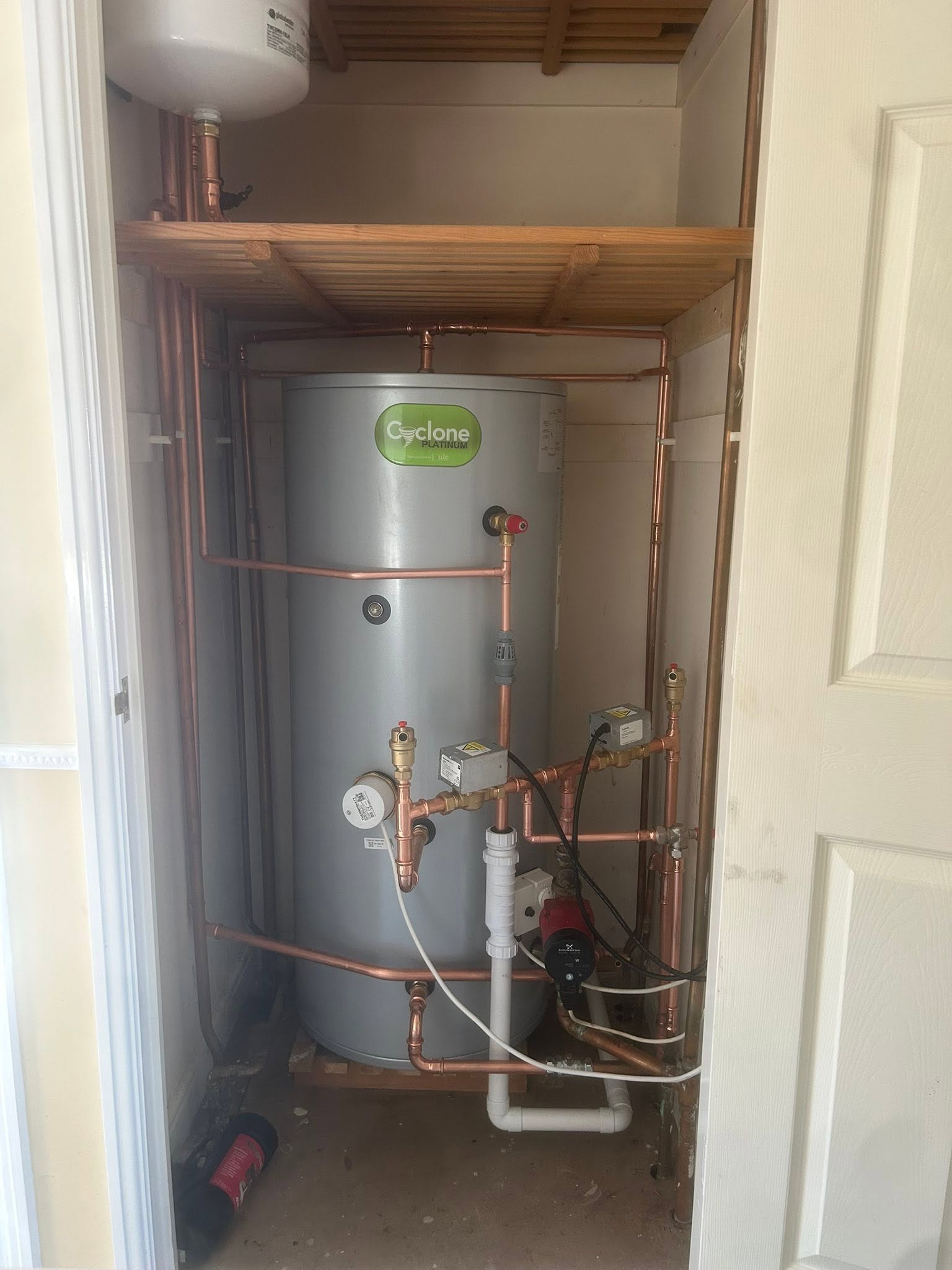 The same cupboard with a new grey unvented cylinder, new copper pipework and a timber shelf above