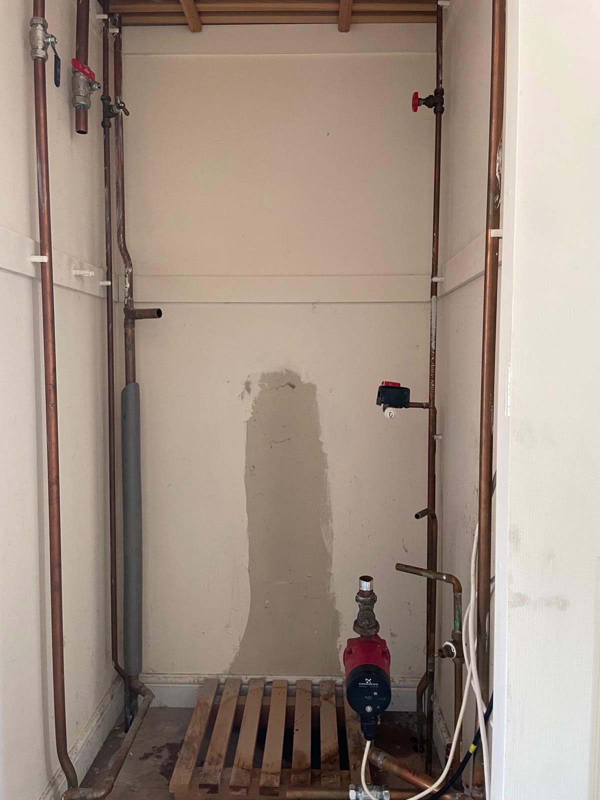The same airing cupboard stripped back, with only the pipework left