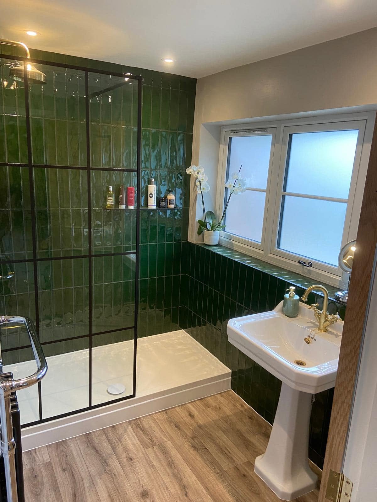 The finished bathroom: green tiles, black grid shower screen and pedestal basin