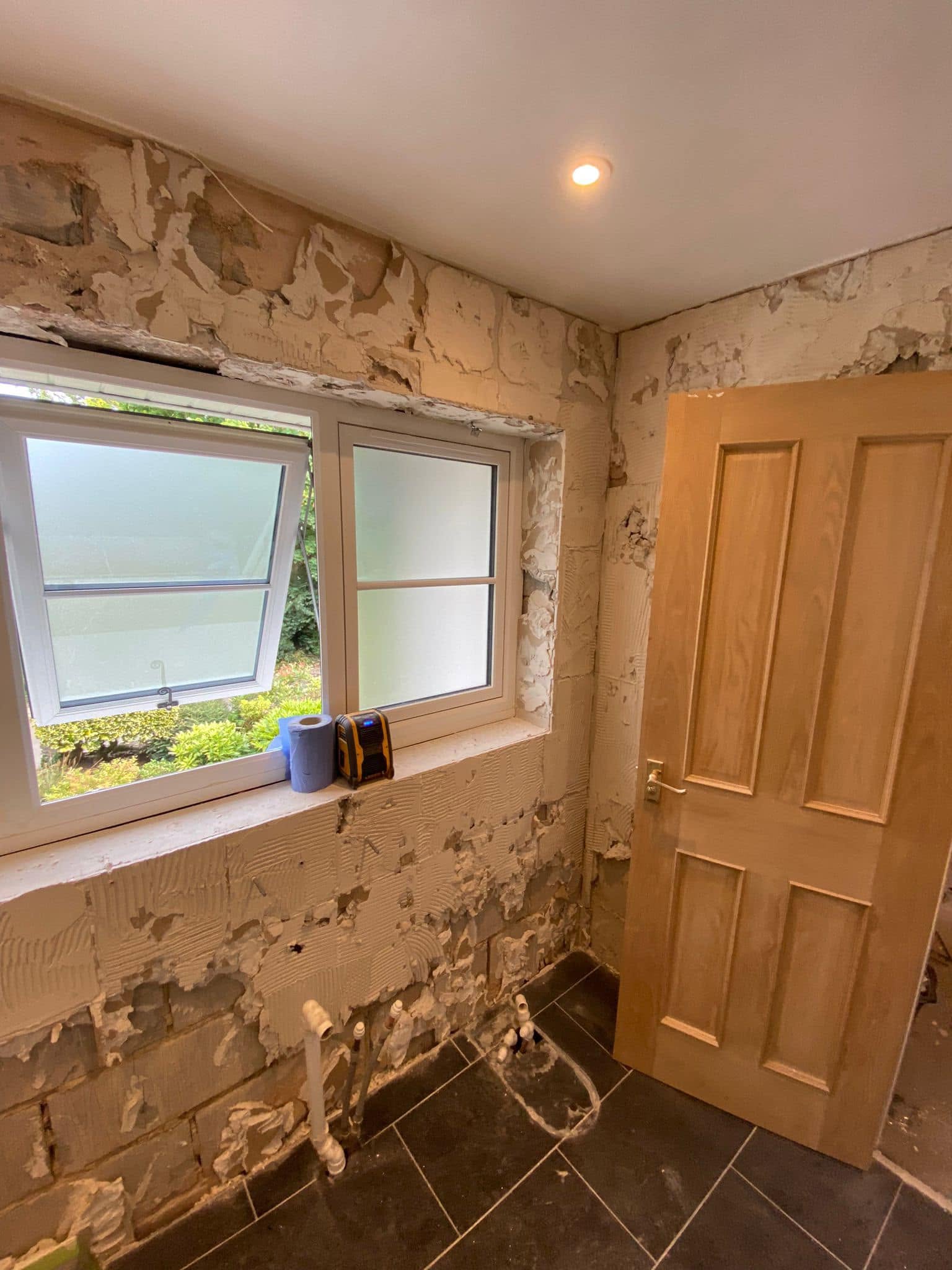 The bathroom before: walls stripped to bare plaster and a slate floor