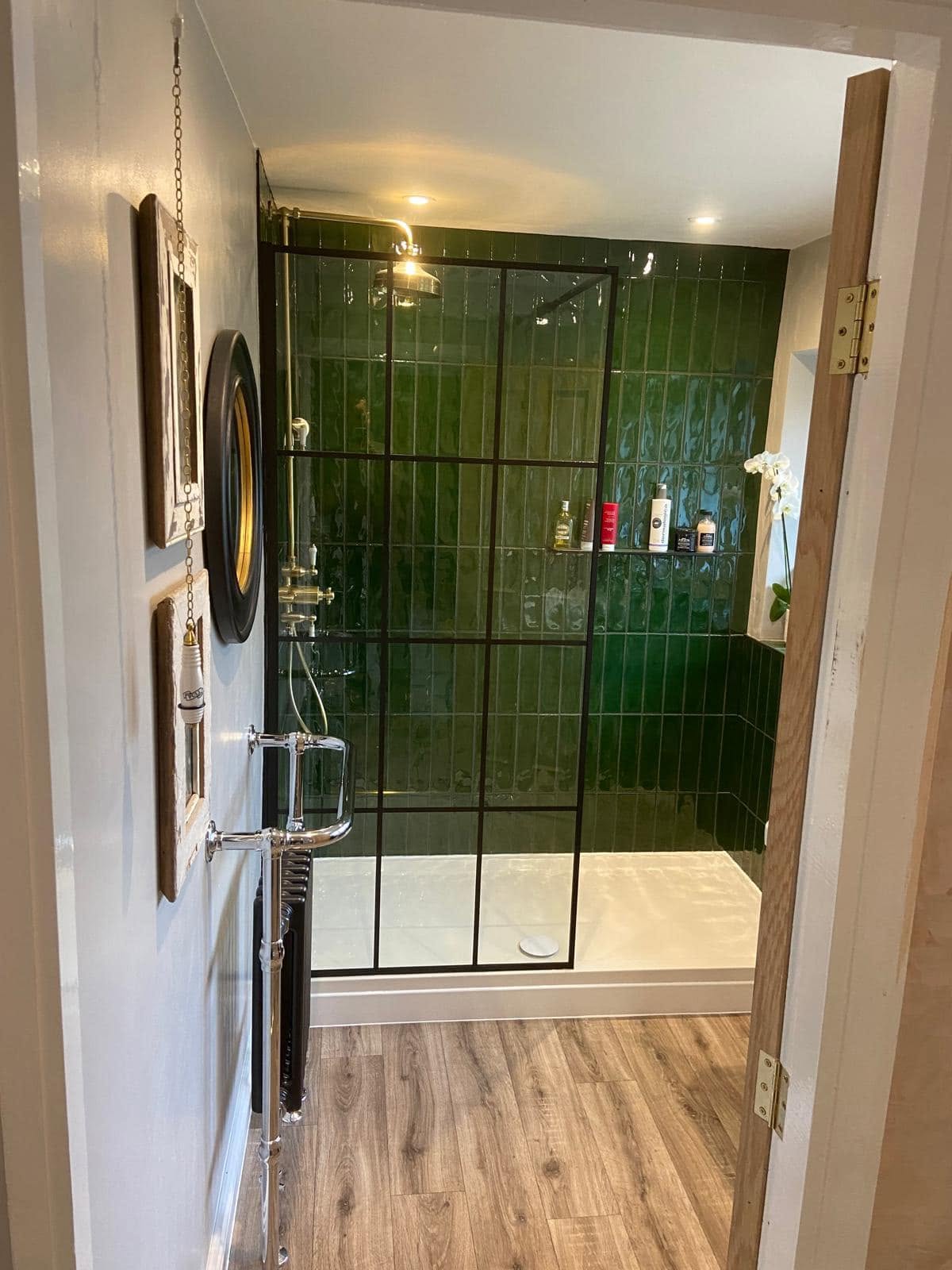 A walk-in shower with a black grid screen and a towel radiator, seen through the bathroom door