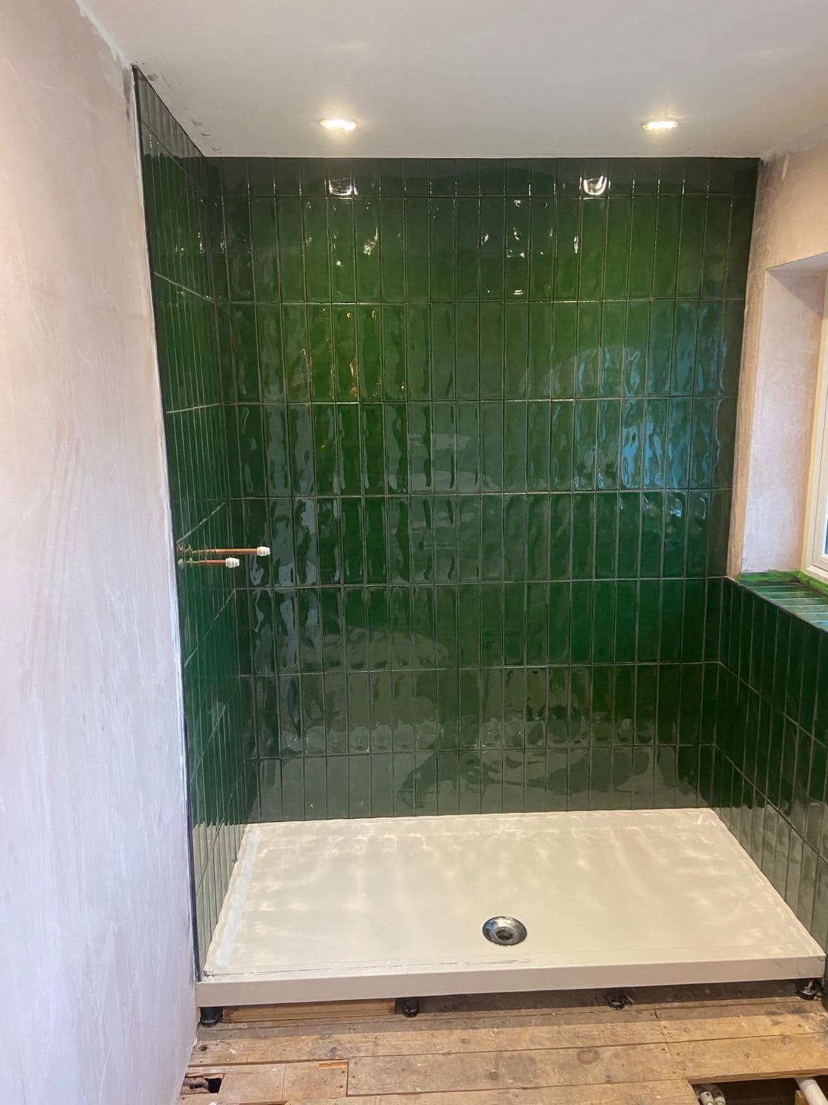 The same bathroom mid-job: green tiles up, shower tray in, floorboards exposed