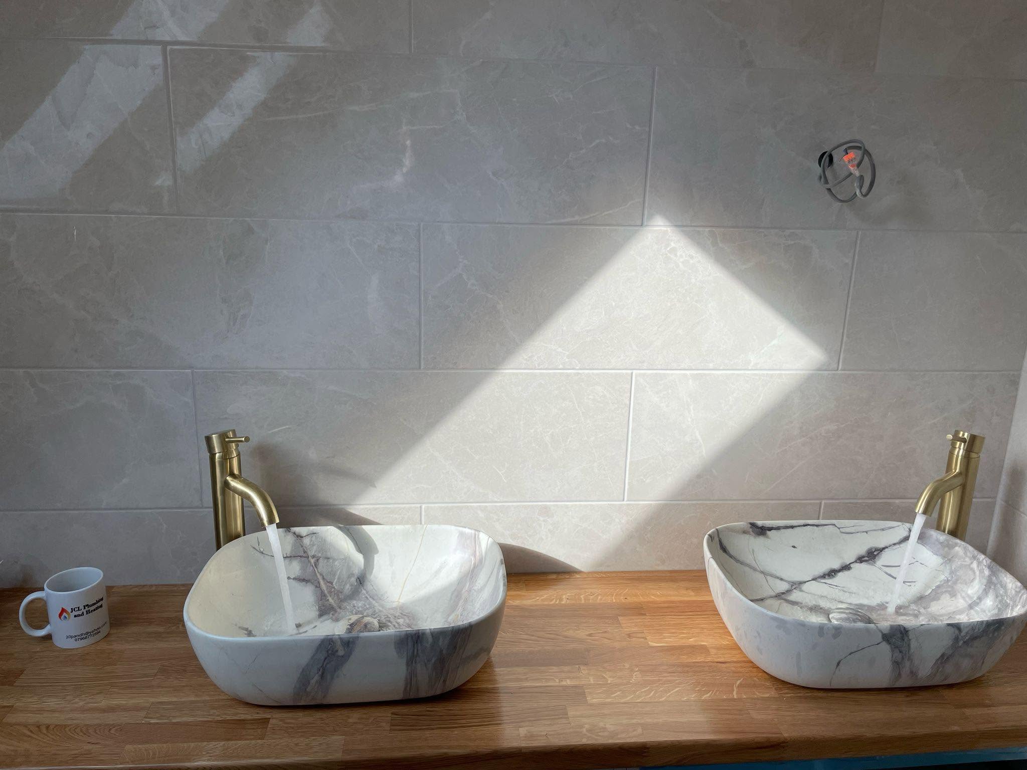 Two marble-effect basins with brushed brass taps on an oak worktop