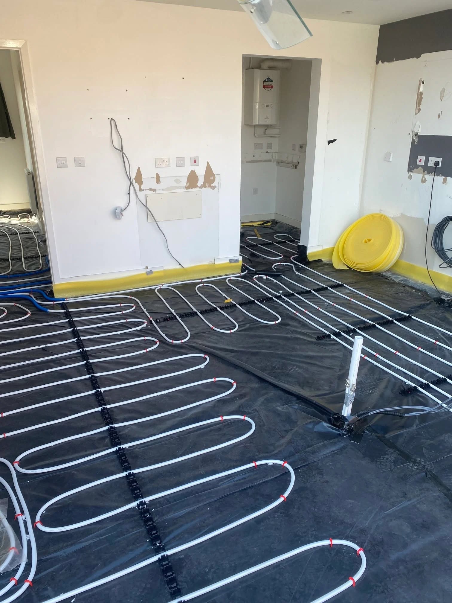 Underfloor heating loops laid through a stripped-out kitchen with the boiler cupboard behind