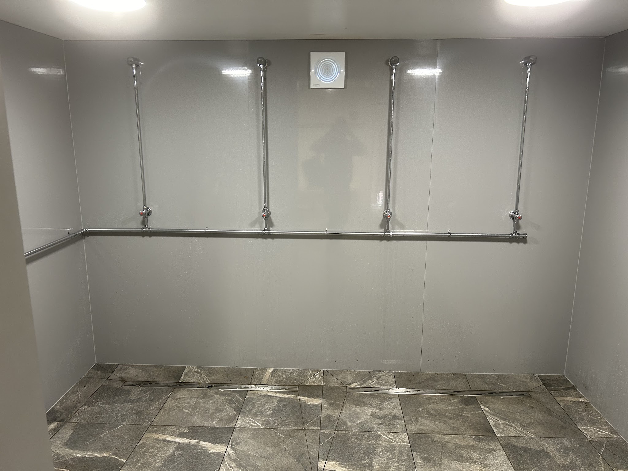 A large panelled shower area with exposed shower risers and stone-effect floor tiles, mid-install
