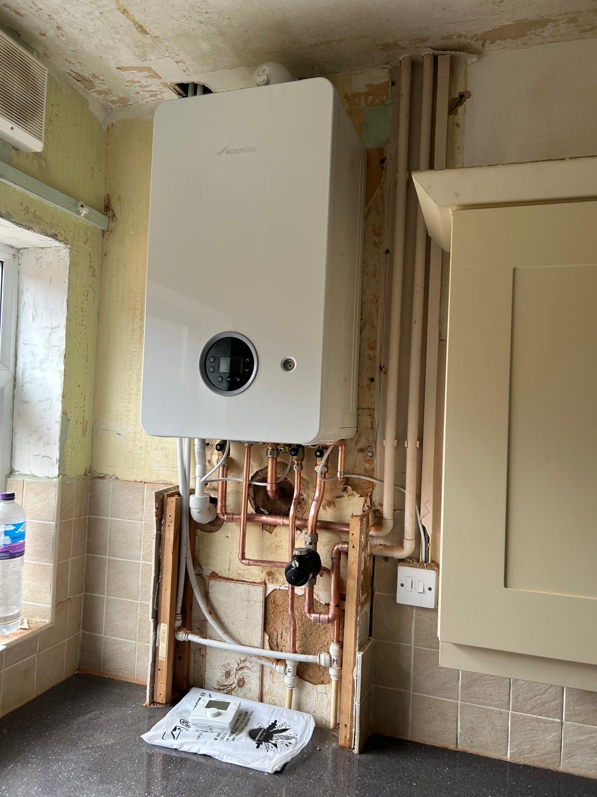 A new white boiler on a kitchen wall, pipework still being boxed in