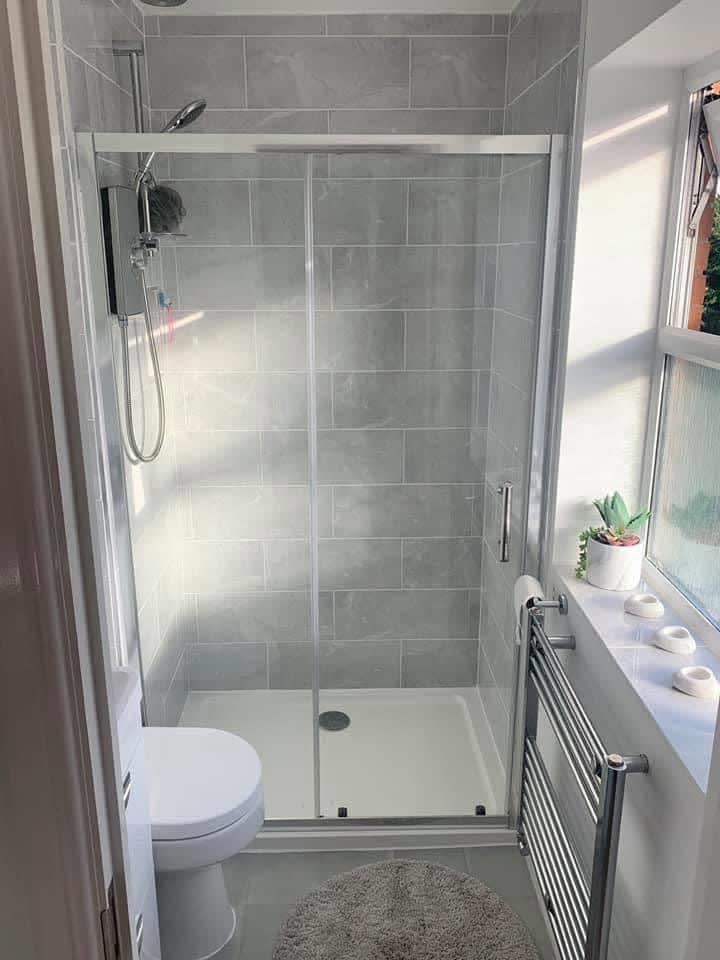A small shower room with a sliding shower door, grey tiles and a chrome towel rail