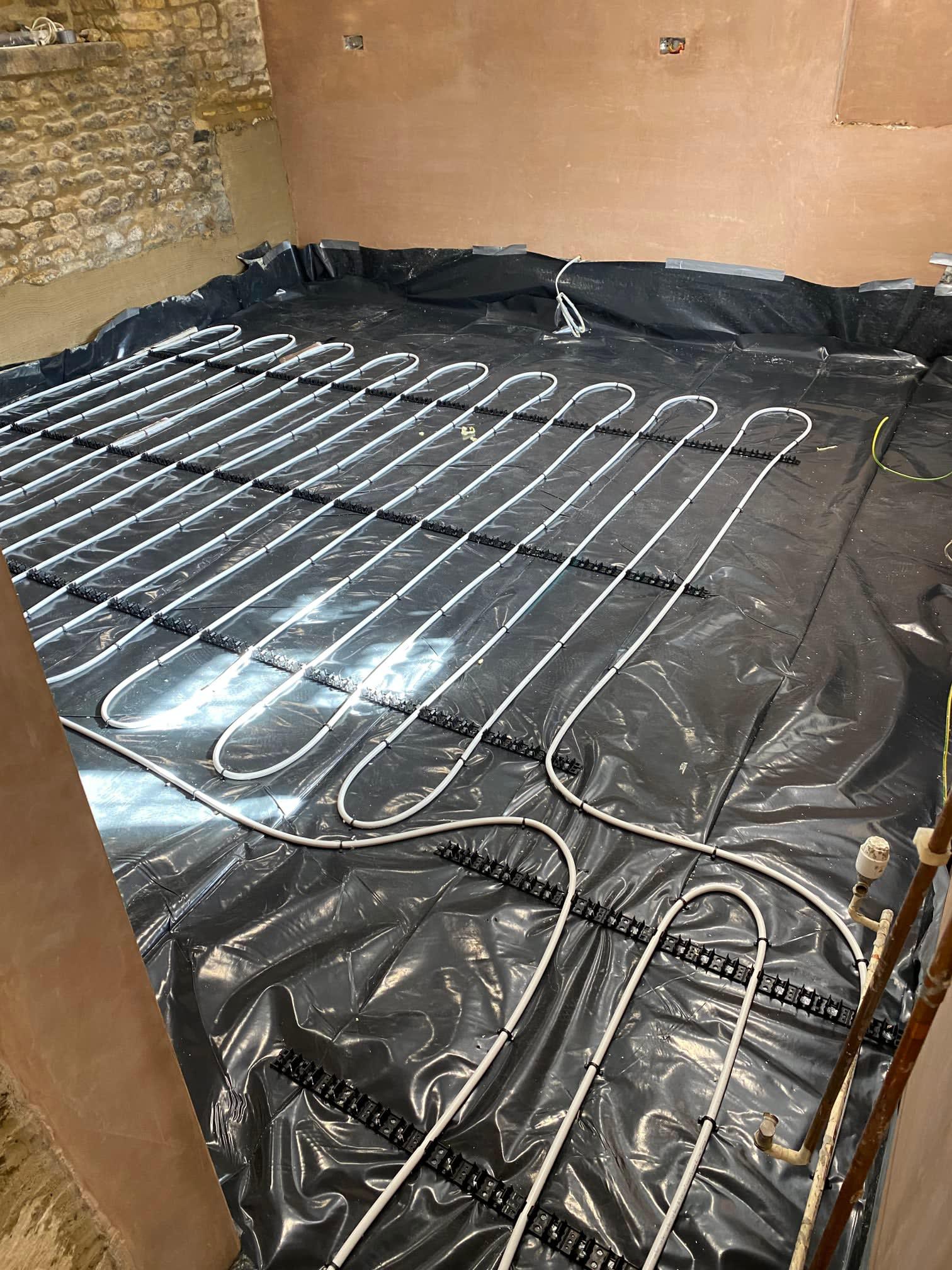 Underfloor heating loops on black membrane in a room with a stone wall