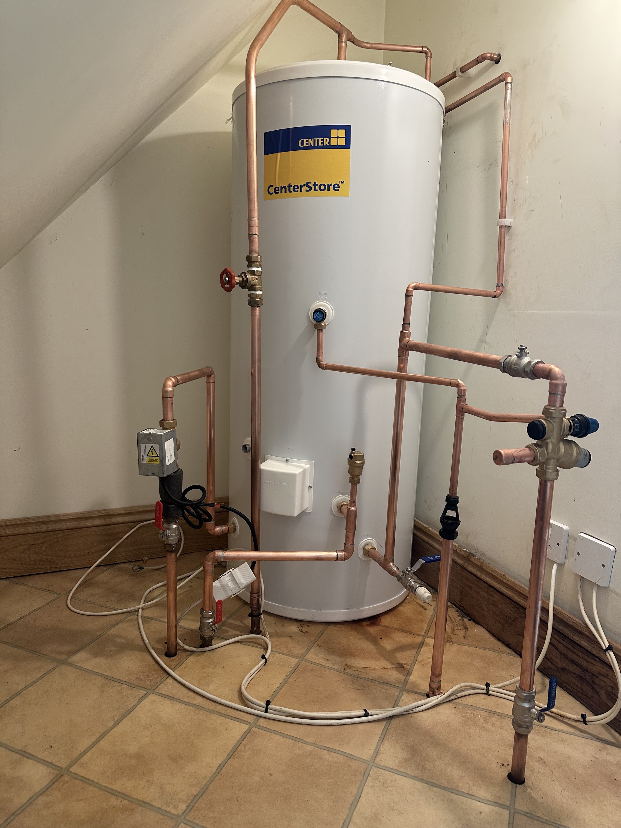 A new white hot water cylinder with copper pipework under a sloping ceiling