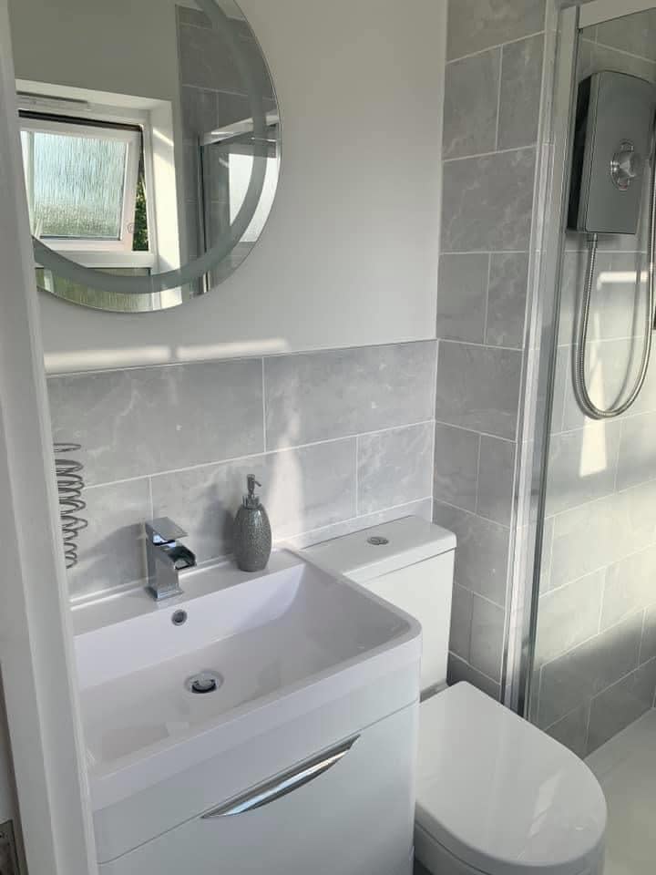 A new bathroom with a vanity basin unit, toilet, electric shower and round mirror