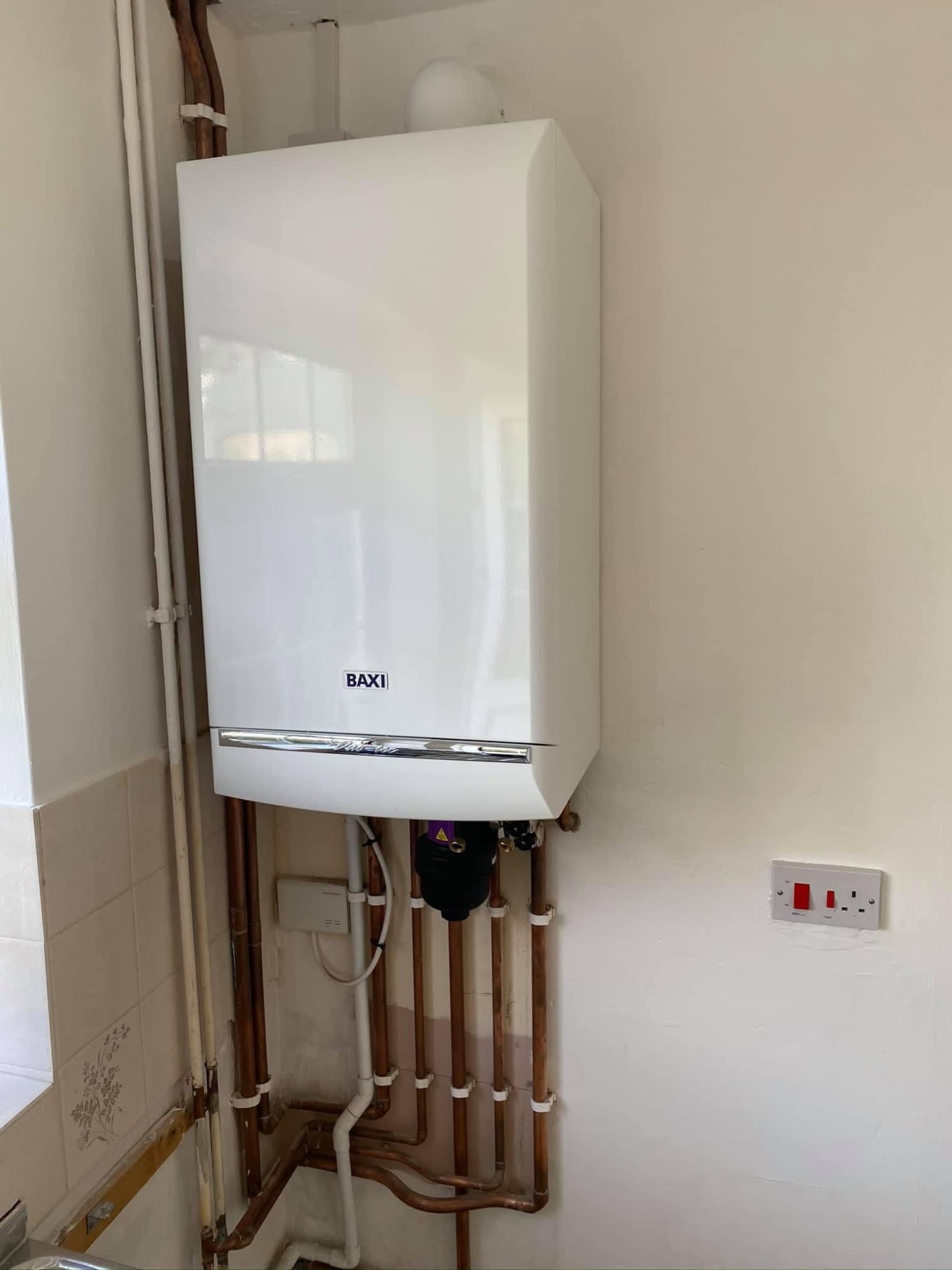 A white Baxi boiler fitted on a kitchen wall with copper pipework below
