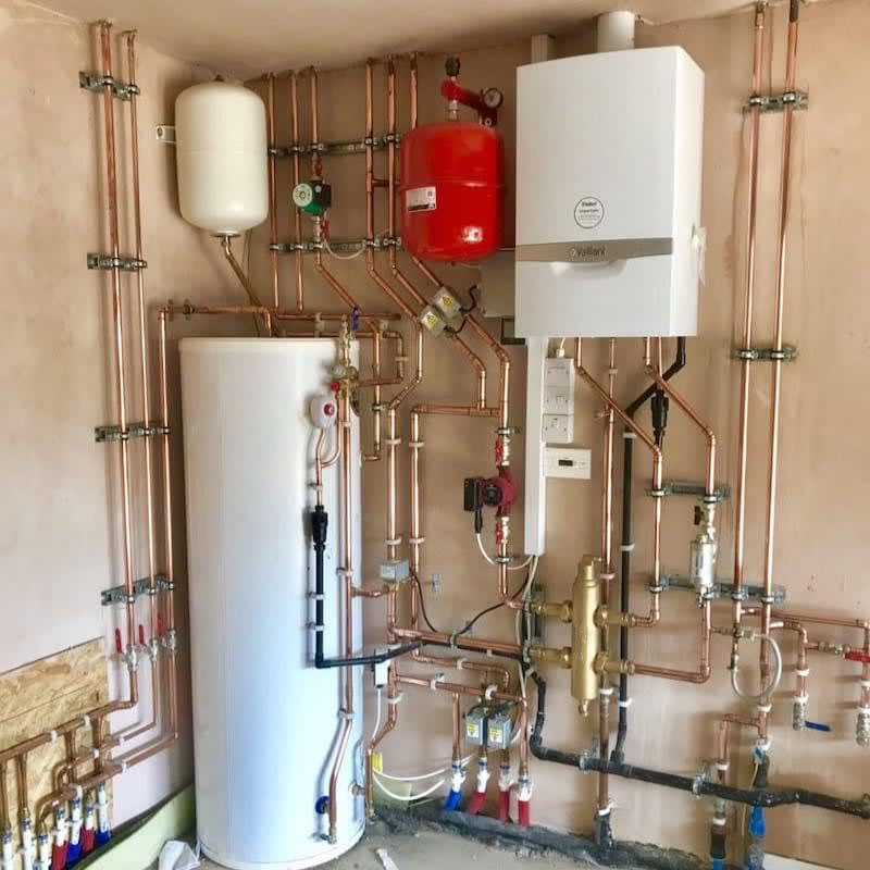 A system boiler, hot water cylinder, expansion vessels and copper pipework in a plant room